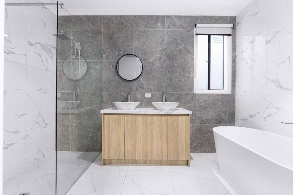 A sleek and stylish modern bathroom with minimalist design, featuring dual washbasins, marble tiles, and a glass shower enclosure.
